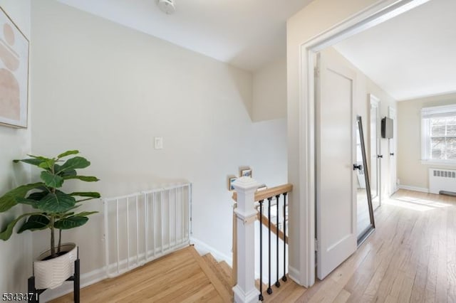 hall featuring light wood-type flooring, an upstairs landing, radiator, and baseboards