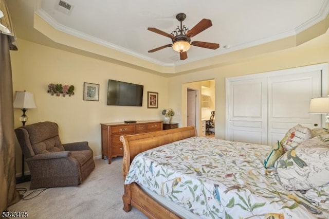 bedroom with visible vents, light colored carpet, a tray ceiling, ornamental molding, and a closet