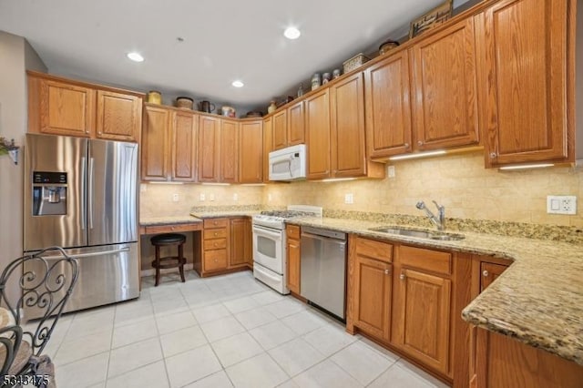 kitchen with light stone counters, a sink, decorative backsplash, appliances with stainless steel finishes, and brown cabinets