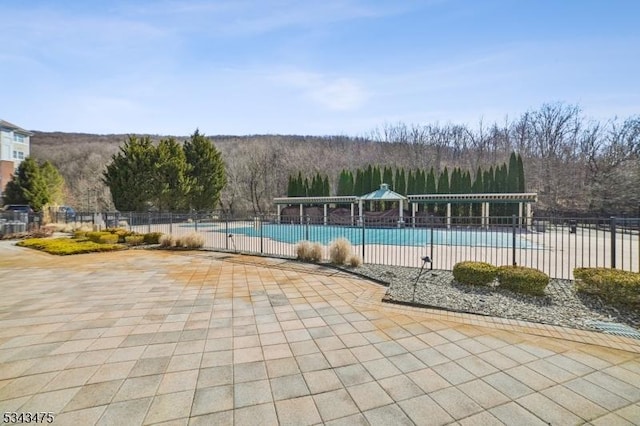 pool with a patio, fence, and a forest view