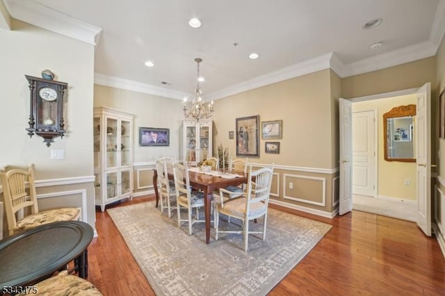 dining area with a wainscoted wall, ornamental molding, an inviting chandelier, wood finished floors, and a decorative wall