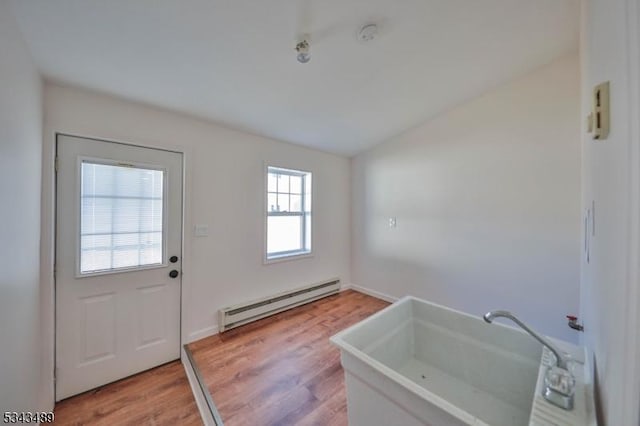 doorway to outside featuring light wood-style flooring, baseboard heating, and a sink