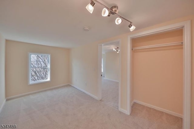 unfurnished bedroom with baseboards, carpet floors, a closet, and rail lighting