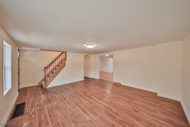 empty room featuring visible vents, light wood-style flooring, stairway, arched walkways, and baseboards