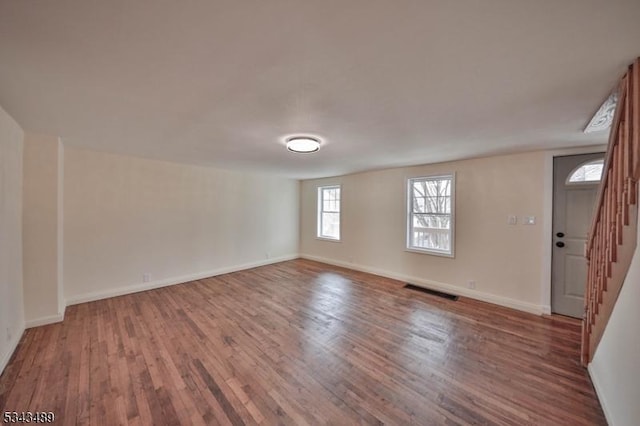 unfurnished room featuring stairs, wood finished floors, visible vents, and baseboards