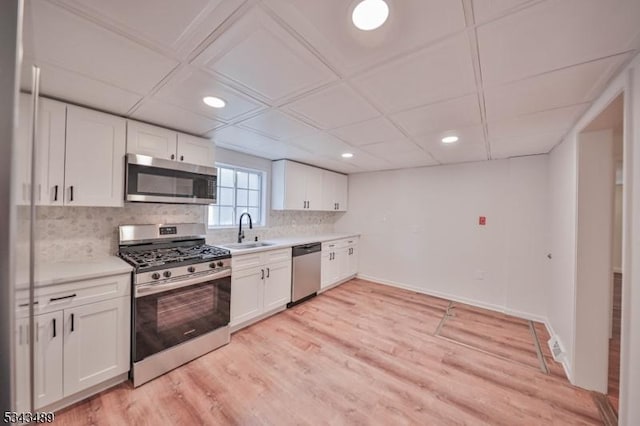 kitchen featuring light countertops, decorative backsplash, appliances with stainless steel finishes, white cabinetry, and a sink