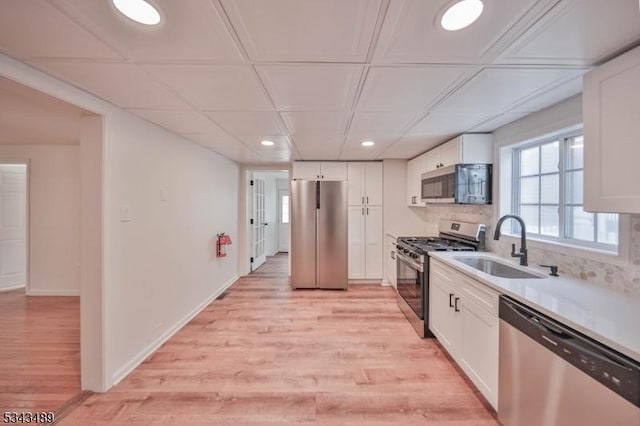 kitchen featuring light wood-style flooring, a sink, appliances with stainless steel finishes, white cabinetry, and backsplash