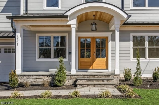 view of exterior entry with a standing seam roof, stone siding, covered porch, an attached garage, and metal roof