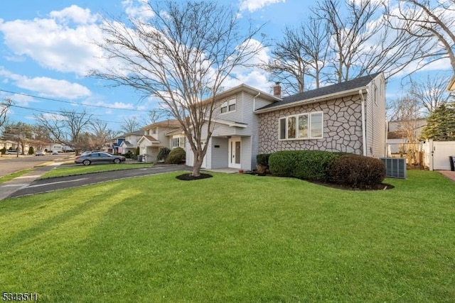 view of front of home with fence, a chimney, a front lawn, stone siding, and aphalt driveway