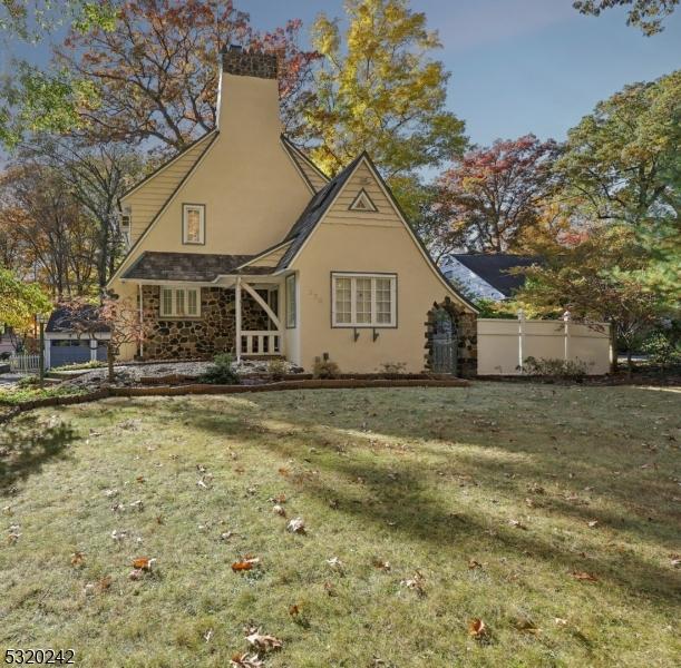 back of house featuring stucco siding, stone siding, a lawn, and a chimney