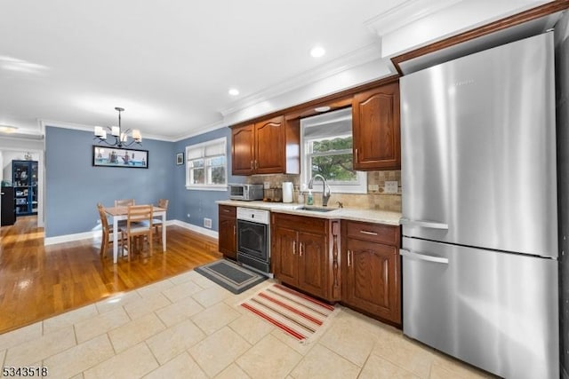 kitchen with a sink, backsplash, freestanding refrigerator, light countertops, and a chandelier