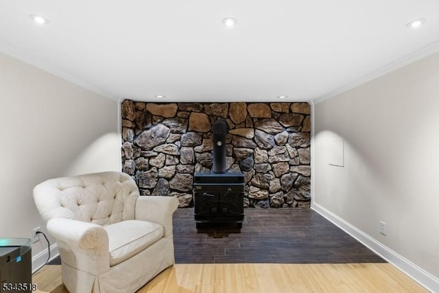 sitting room with baseboards, ornamental molding, recessed lighting, a wood stove, and wood finished floors