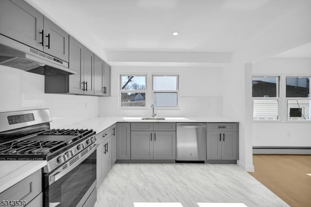 kitchen with under cabinet range hood, baseboard heating, gray cabinets, stainless steel appliances, and a sink