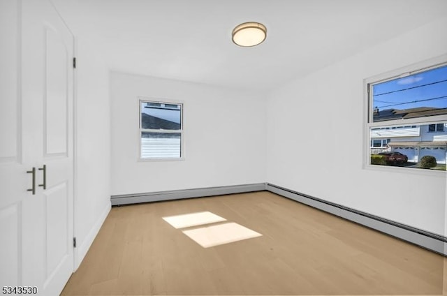 spare room featuring a baseboard heating unit, wood finished floors, and baseboards