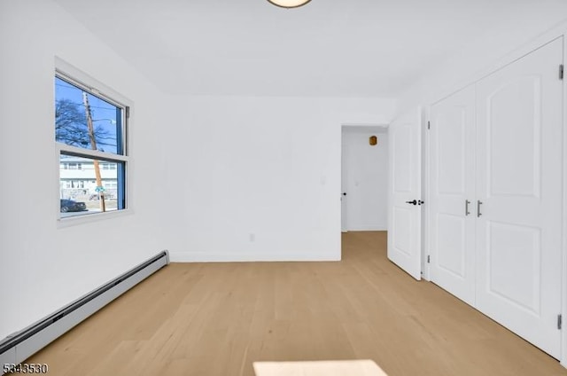 unfurnished bedroom featuring a baseboard radiator, baseboards, a closet, and light wood-style flooring