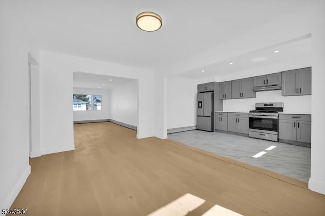 kitchen with gray cabinetry, under cabinet range hood, light wood-style floors, appliances with stainless steel finishes, and light countertops