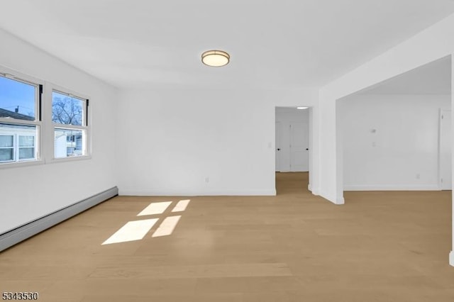 spare room with a baseboard radiator, baseboards, and light wood-style flooring