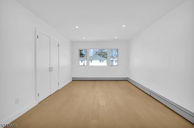 empty room with recessed lighting, light wood-style flooring, a baseboard heating unit, and baseboards