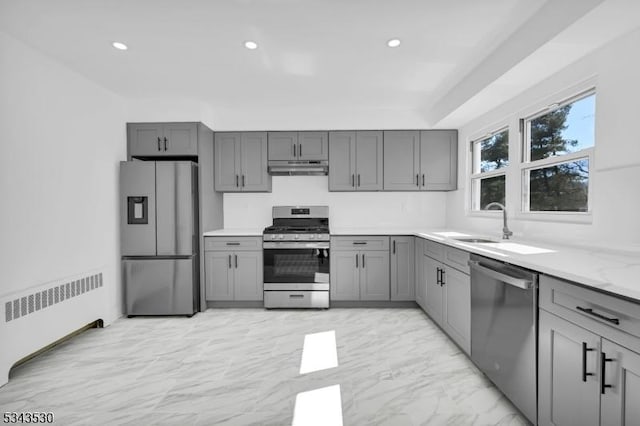 kitchen with marble finish floor, gray cabinetry, under cabinet range hood, radiator heating unit, and appliances with stainless steel finishes