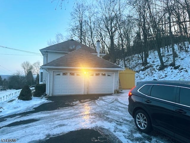 view of snowy exterior featuring a chimney and a detached garage