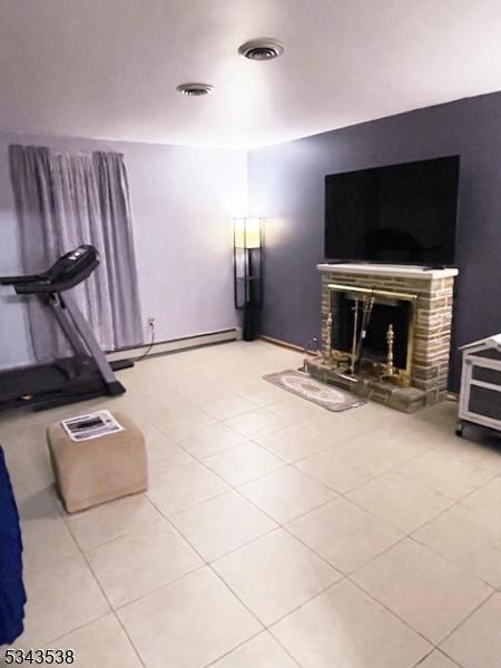 unfurnished living room with tile patterned floors, visible vents, baseboard heating, and a fireplace with raised hearth