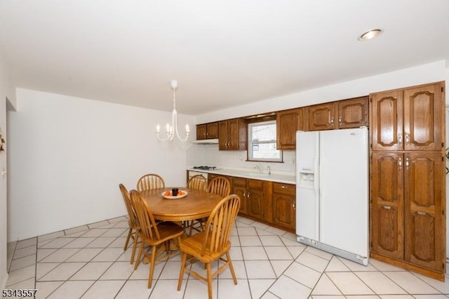 kitchen with a notable chandelier, gas cooktop, tasteful backsplash, white fridge with ice dispenser, and light countertops