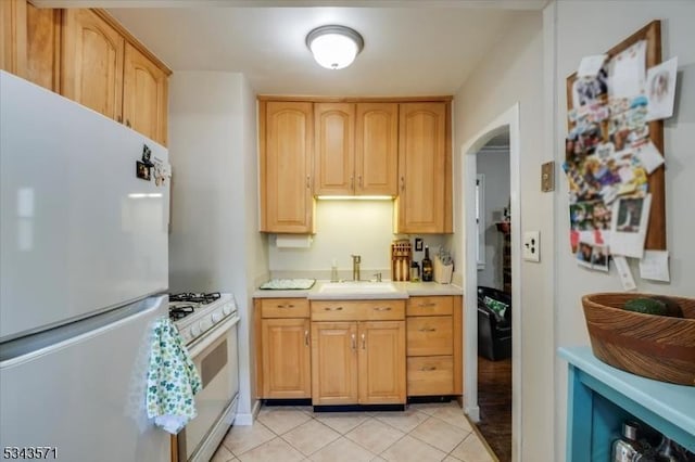 kitchen featuring light countertops, light tile patterned floors, arched walkways, white appliances, and a sink