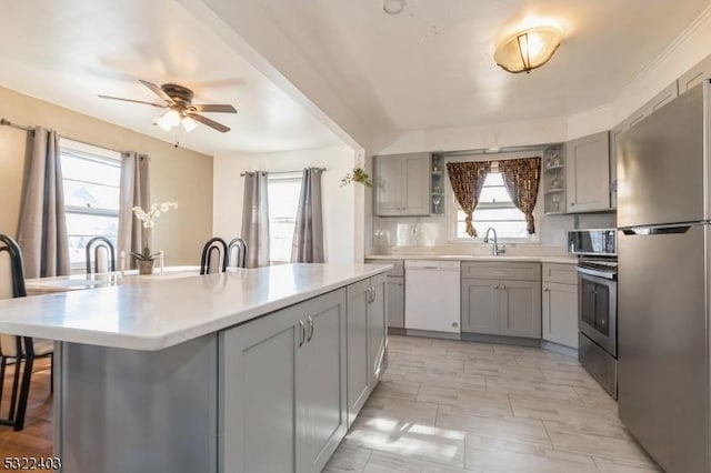 kitchen with a ceiling fan, a kitchen island with sink, appliances with stainless steel finishes, and gray cabinetry