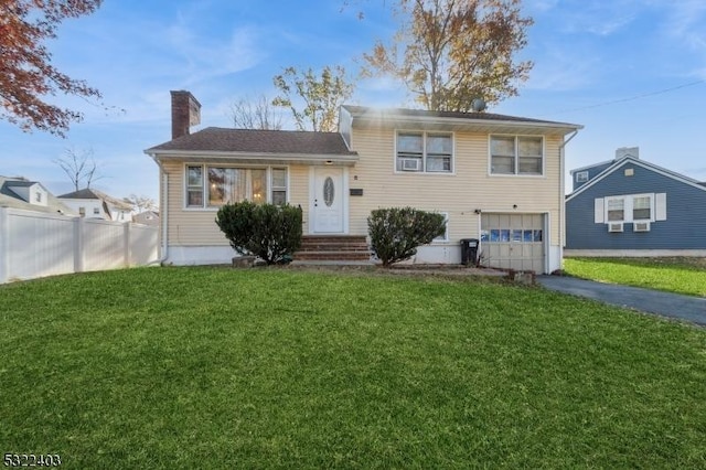 split level home featuring driveway, a front lawn, fence, a garage, and a chimney