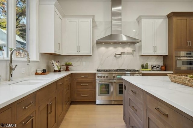 kitchen featuring tasteful backsplash, appliances with stainless steel finishes, white cabinetry, wall chimney exhaust hood, and a sink