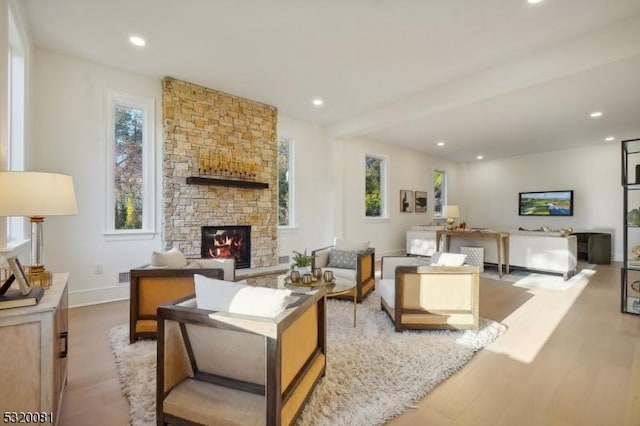 living room featuring a stone fireplace, recessed lighting, baseboards, and wood finished floors