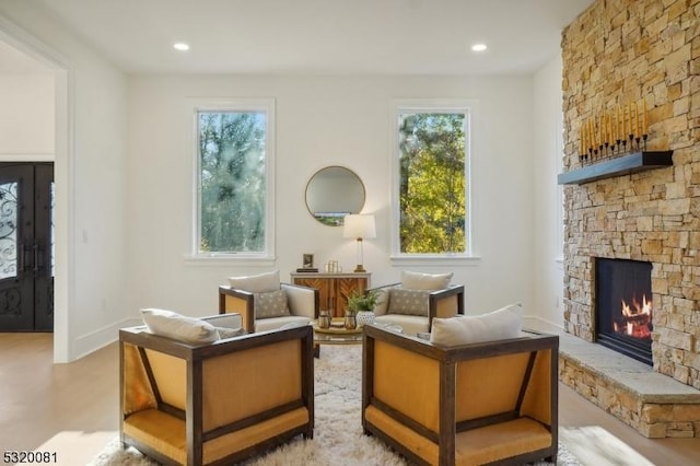 living area featuring recessed lighting, baseboards, a stone fireplace, and wood finished floors