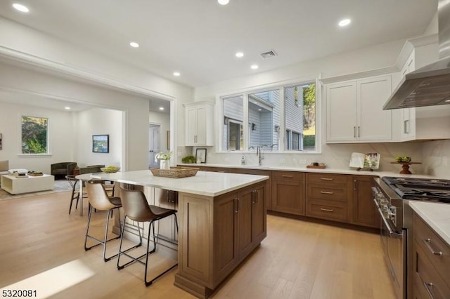 kitchen featuring a kitchen island, a breakfast bar area, stainless steel stove, white cabinets, and wall chimney exhaust hood