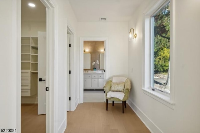 hall with a wealth of natural light, visible vents, light wood-style flooring, and baseboards