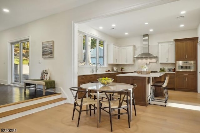 kitchen featuring a kitchen island, a sink, oven, wall chimney range hood, and light wood-type flooring