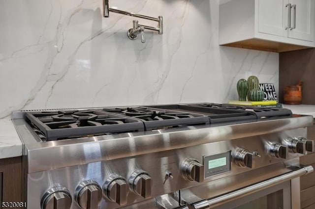 room details featuring backsplash, white cabinets, stainless steel range with gas cooktop, and light stone countertops