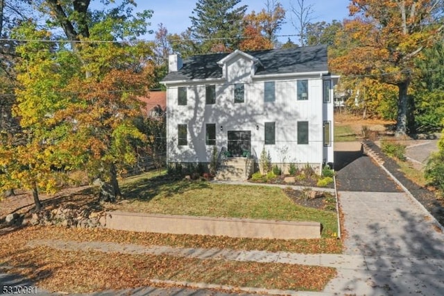 colonial house featuring aphalt driveway, a chimney, and a front lawn