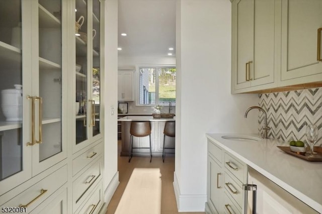 kitchen with recessed lighting, a sink, light countertops, glass insert cabinets, and backsplash