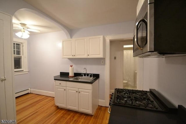 kitchen featuring light wood-type flooring, a sink, stainless steel microwave, a baseboard heating unit, and gas stove