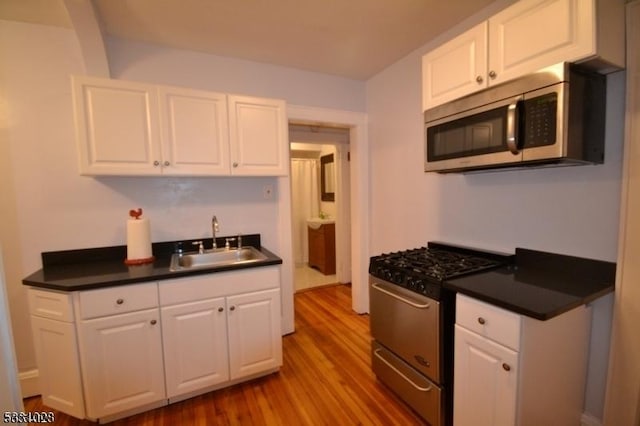 kitchen featuring a sink, dark countertops, wood finished floors, white cabinetry, and stainless steel appliances