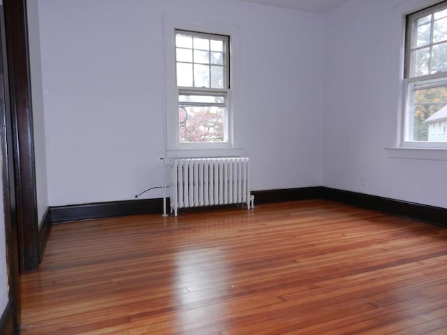 empty room featuring radiator heating unit, baseboards, and hardwood / wood-style floors