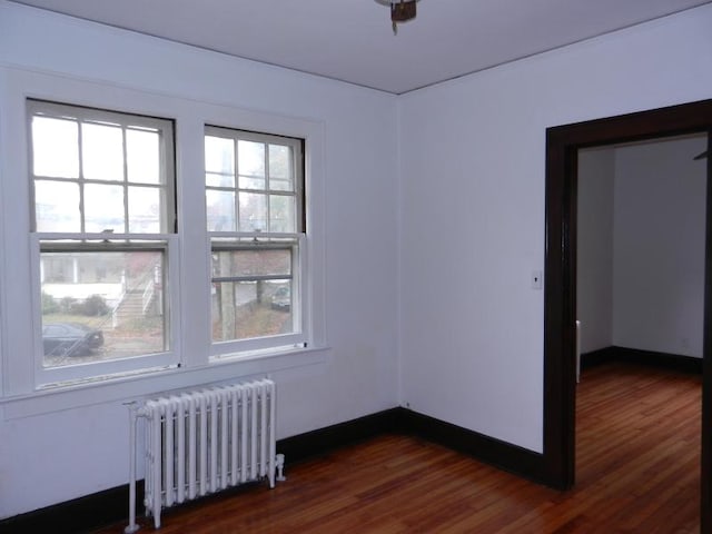 spare room with baseboards, dark wood finished floors, and radiator heating unit