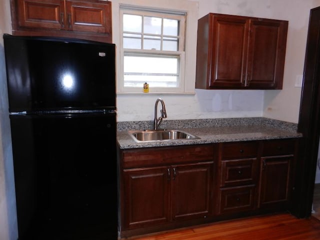 kitchen with light stone countertops, wood finished floors, freestanding refrigerator, a sink, and dark brown cabinetry