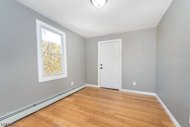 unfurnished room featuring baseboards, light wood finished floors, and a baseboard radiator