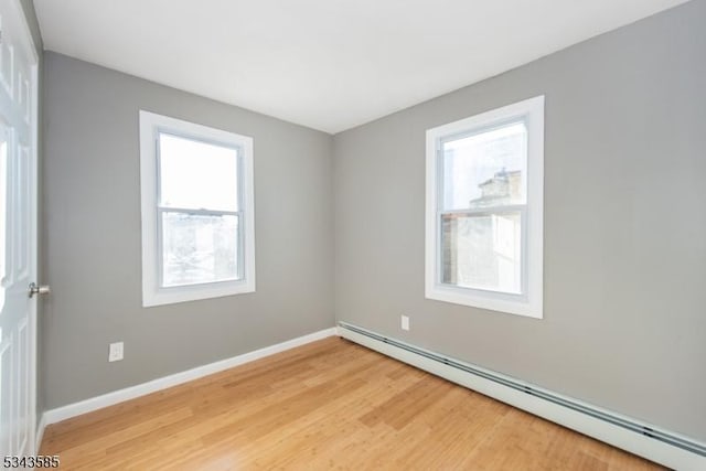 empty room featuring baseboards, baseboard heating, and light wood finished floors