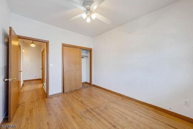 unfurnished bedroom featuring a baseboard heating unit, ceiling fan, baseboards, light wood-style floors, and a closet