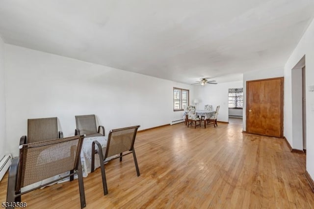 living area featuring a ceiling fan, baseboards, and light wood finished floors