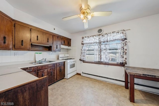 kitchen with white range with gas cooktop, a ceiling fan, under cabinet range hood, a sink, and baseboard heating