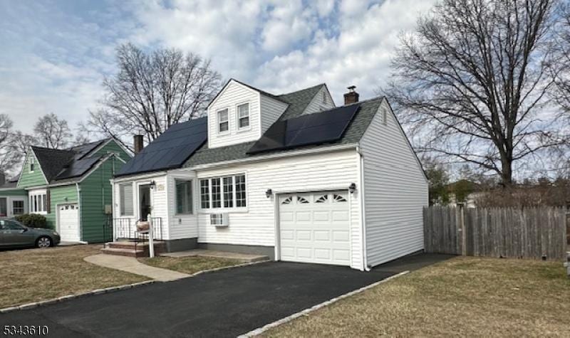cape cod house with solar panels, fence, aphalt driveway, a chimney, and an attached garage