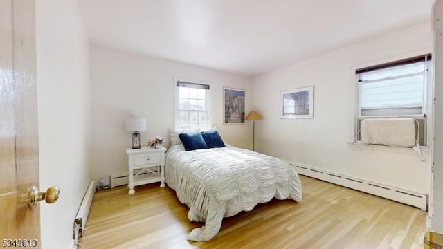 bedroom with a baseboard radiator and light wood-style flooring